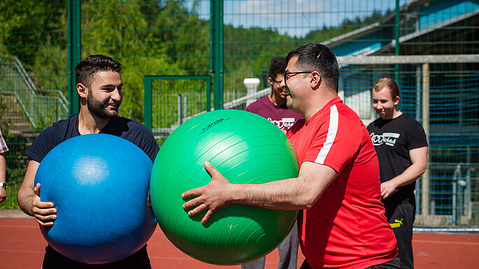 zwei sich gegenüberstehende Personen halten einen Gymnastikball in der Hand 