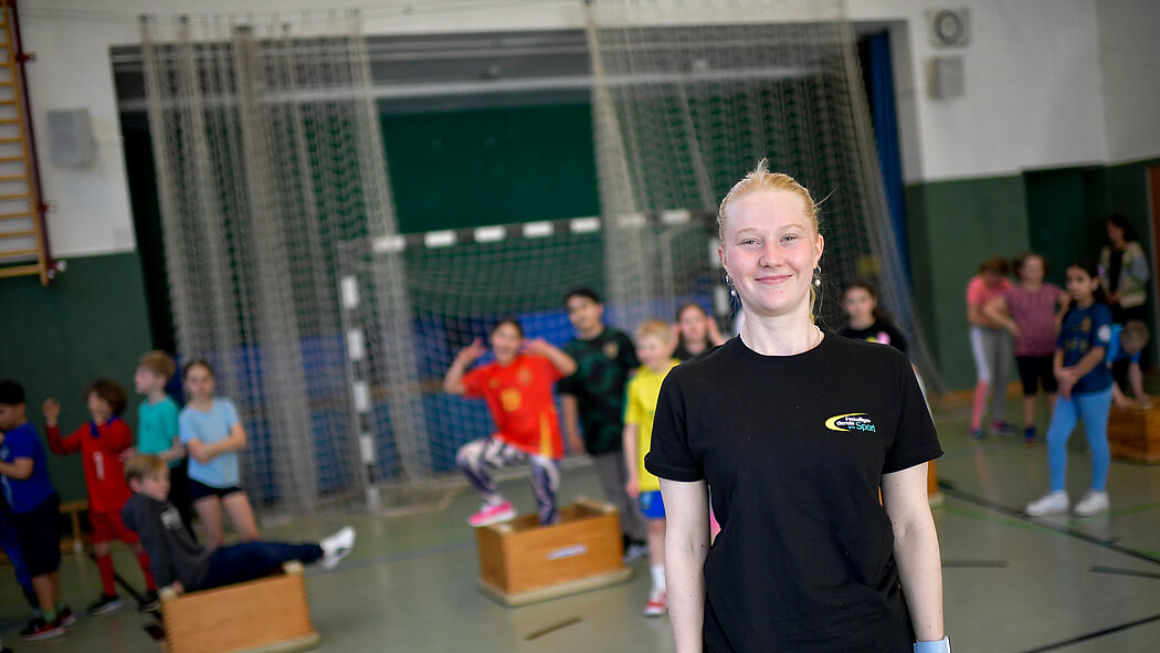 Eine junge Trainerin steht in einer Turnhalle vor einer Menge Kinder