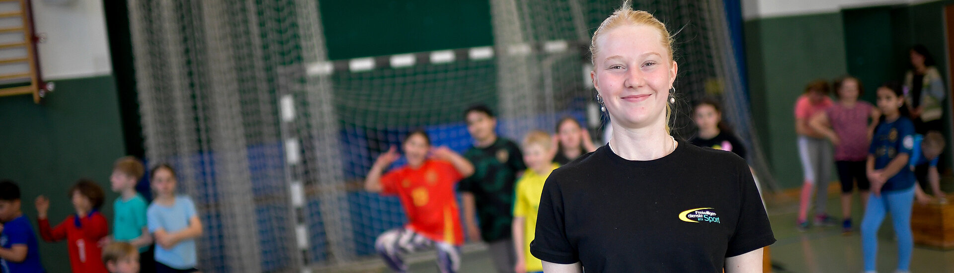 Eine junge Trainerin steht in einer Turnhalle vor einer Menge Kinder